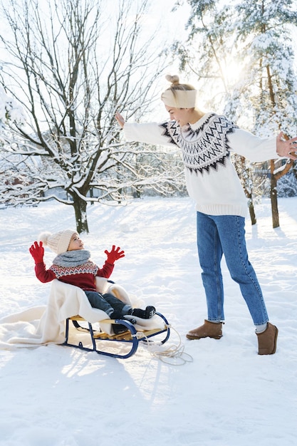 写真 晴れた冬の日の雪の公園でレトロなそりと若い母親と彼女のかわいい幼い息子