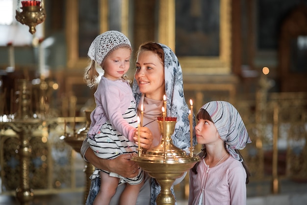 Фото Молодая мать и ее маленькая белокурая кавказская дочь со свечами в православной русской церкви