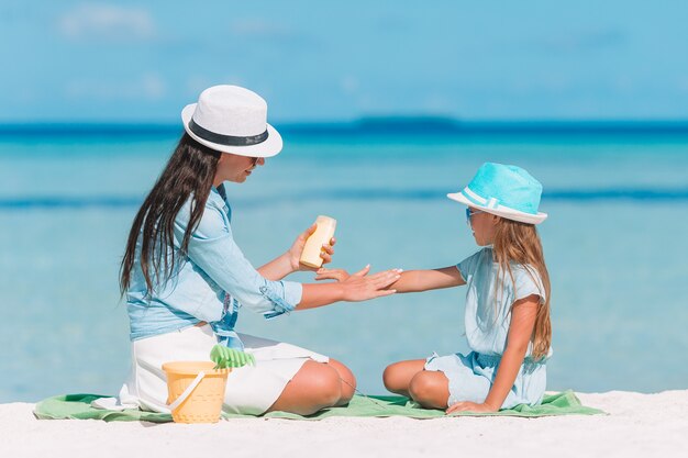 Young mother applying sun cream to daughter on the beach