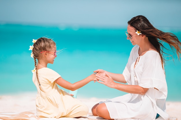 Young mother applying sun cream to daughter nose on the beach. Sun protection