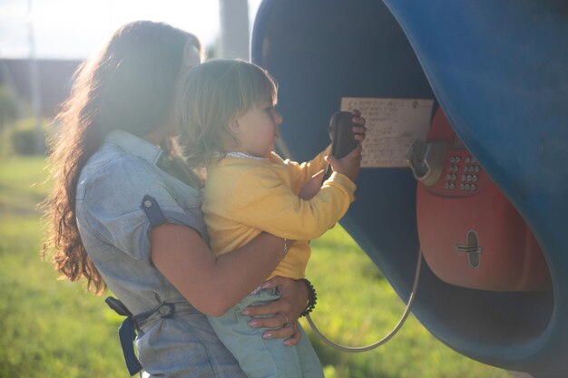 La giovane madre e il bambino chiamano su un telefono fisso su strada nella cabina telefonica del villaggio in estate