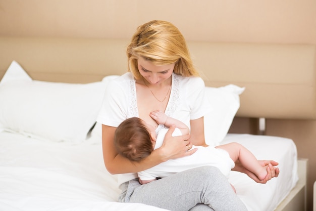 A young mother breastfeeding her little baby girl while holding in her arms