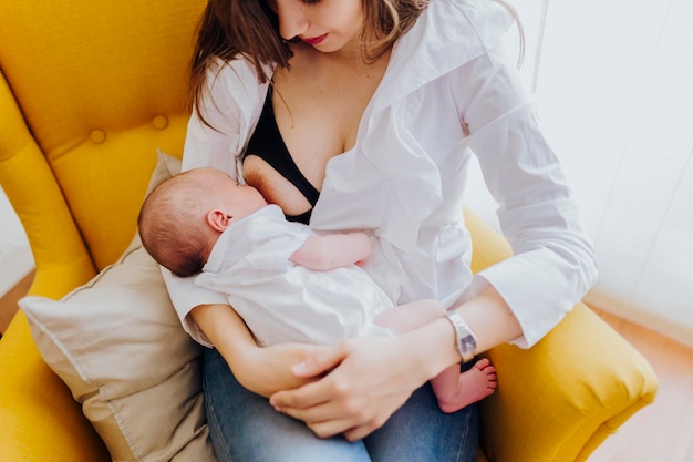 Young mother breastfeeding her newborn baby boy sitting on yellow armchair