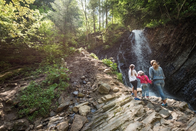 Young mother and children walk through the woods with a bewitching view of the natural expanses of the hills rock formations and a waterfall