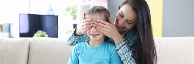 Young mother closes her daughter eyes and gives her gift