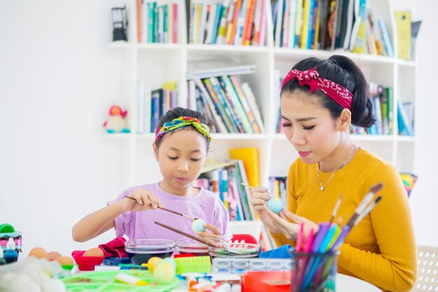 Photo young mother colors easter eggs with her daughter