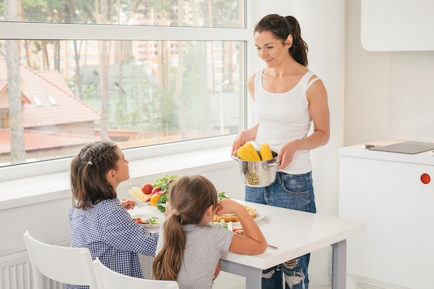 若い母親が子供のためのおいしいトウモロコシを調理