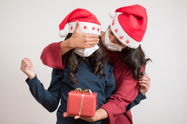 Foto giovane madre che copre gli occhi a sua figlia che dà un regalo rosso per natale.