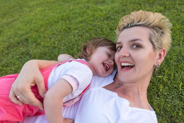 Foto giovane madre e figlia carina che si godono il tempo libero giocando all'aperto in cortile sull'erba, famiglia felice nel concetto di natura