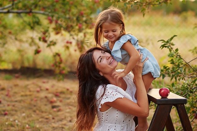 Young mother and daughter in the apple orchard harvest