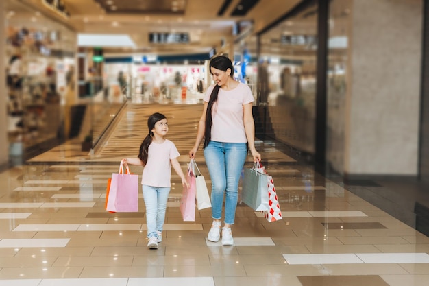 Young mother and daughter holding shopping bags shopping in the mall Family shopping