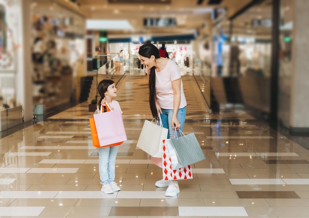 Young mother and daughter holding shopping bags shopping in the mall Family shopping