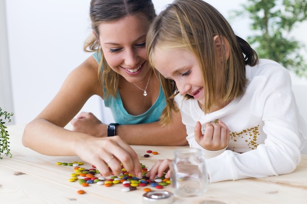 Young mother and daughter playing with sweets at home.