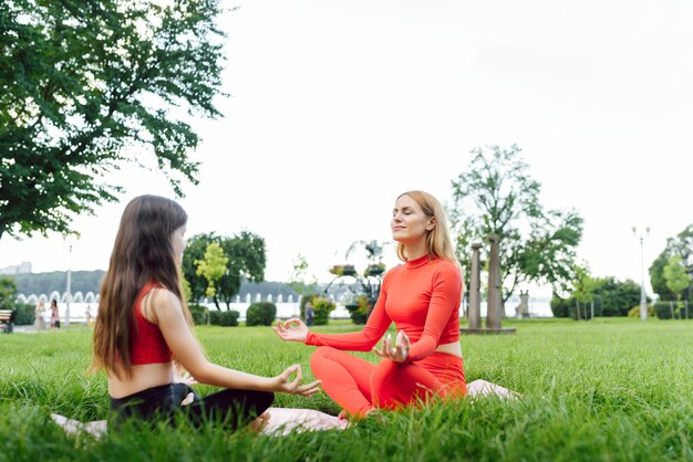 A young mother and daughter in sportswear do yoga together in a Park