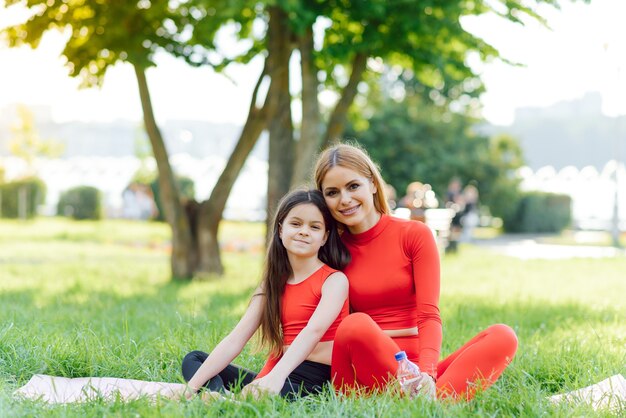 A young mother and daughter in sportswear do yoga together in a Park