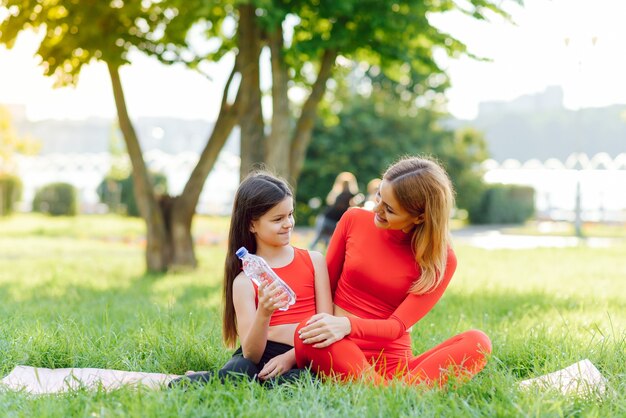 A young mother and daughter in sportswear do yoga together in a Park