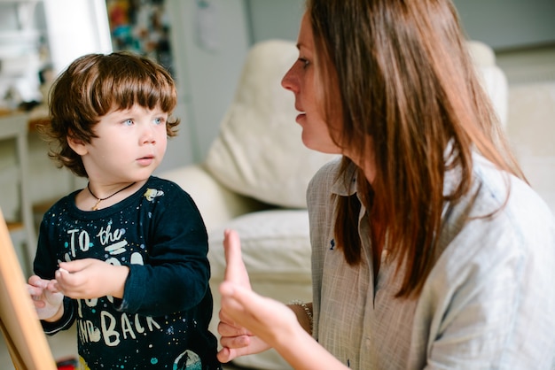 Foto giovane madre disegno gesso sulla lavagna con il suo giovane figlio a casa