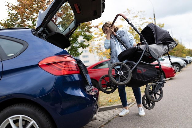 Young mother driver puts a baby stroller into the luggage compartment of the car