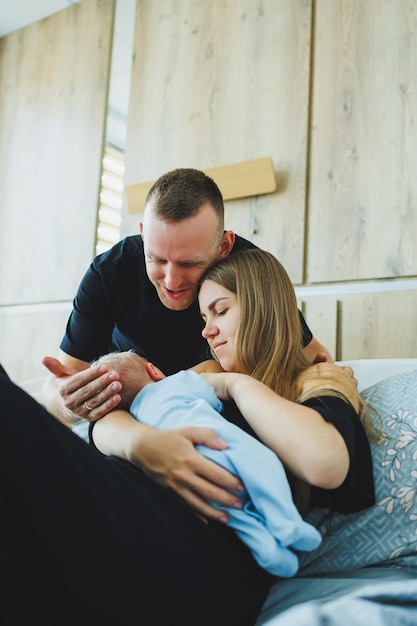 A young mother and father hug their newborn son a woman breastfeeds her child The first day of young parents after the birth of a child