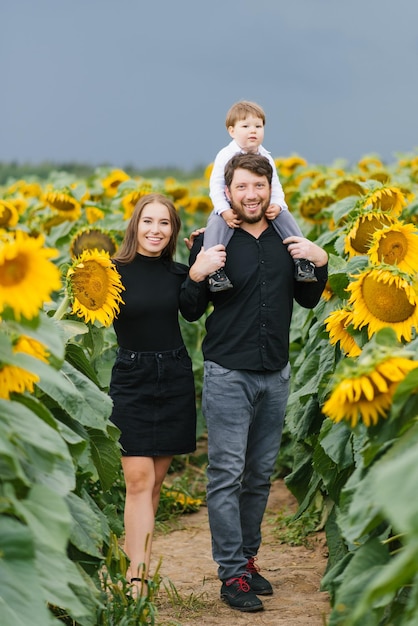 A young mother and father with their young son walking through a field with sunflowers