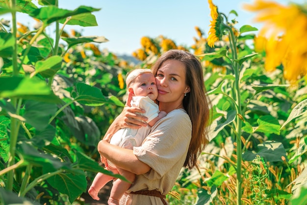 A young mother gently cuddles a cute little baby in a field of sunflowers.