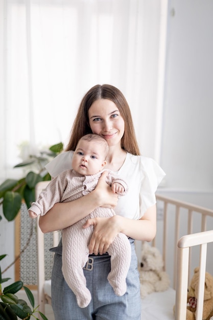 A young mother gently embraces her little baby girl holding him in her arms at home in the bedroom of the nursery by the bed closeup Portrait of a happy mother and a newborn baby