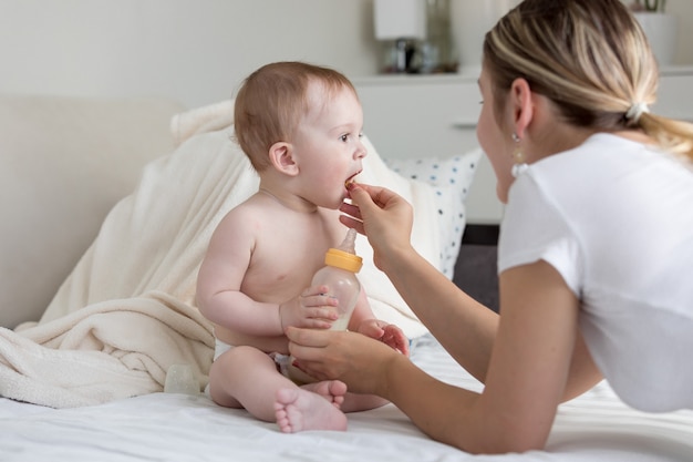 Young mother giving baby cookies to her 9 months old son sitting on bed