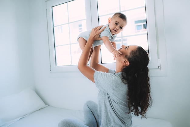 Giovane madre che si diverte con il suo bambino a letto a casa - focus sui volti