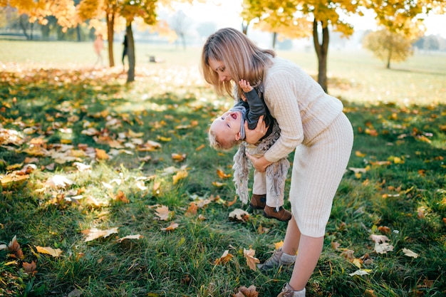 日当たりの良い秋の公園で彼女の肩に小さな子供を楽しんで若い母親。