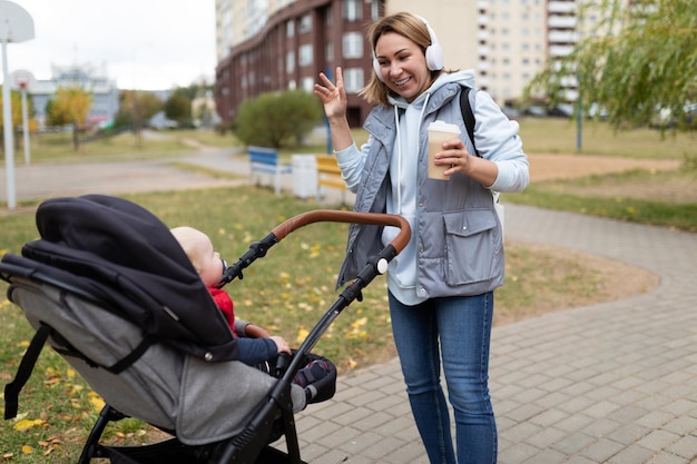 Молодая мама в наушниках гуляет с детской коляской в парке