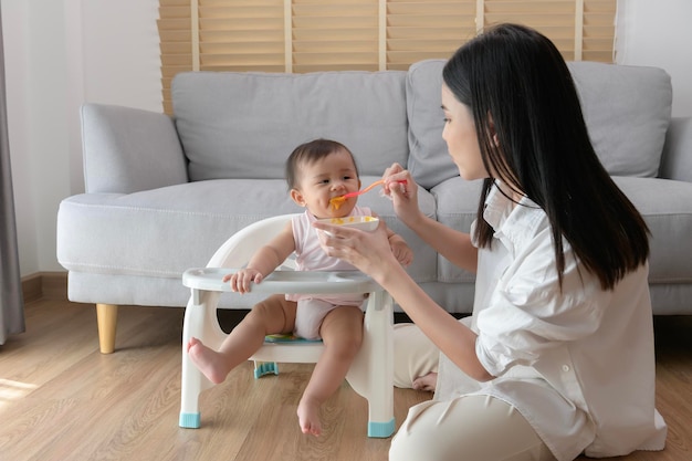 Giovane madre che aiuta il bambino a mangiare cibo misto sulla sedia del bambino