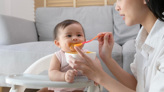 赤ちゃんがベビーチェアでブレンド食品を食べるのを助ける若い母親