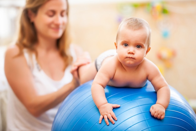 Young mother helping little baby practicing gymnastic exercises at home