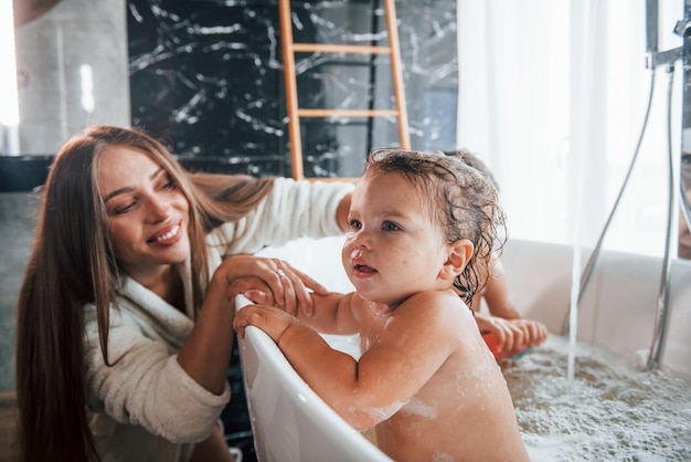 Young mother helps her son and daughter Two kids washing in the bath