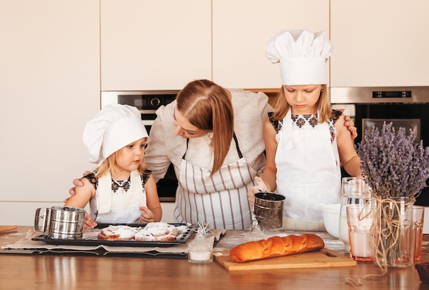 Young mother helps her two daughters cook dough in the kitchen