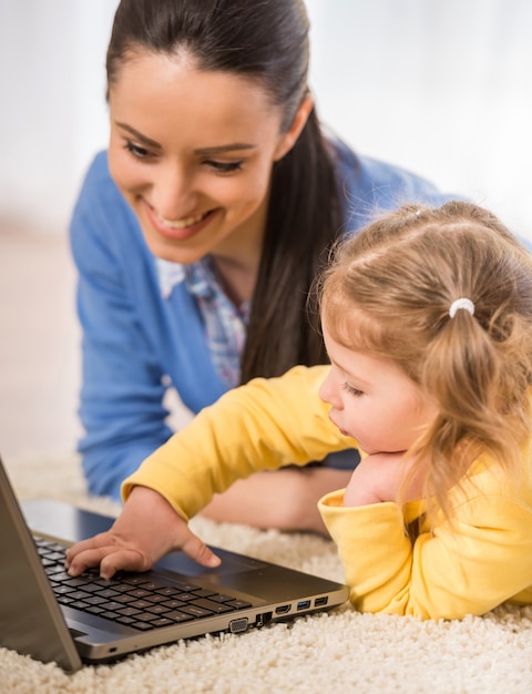 Young mother and her adorable daughter are using laptop.