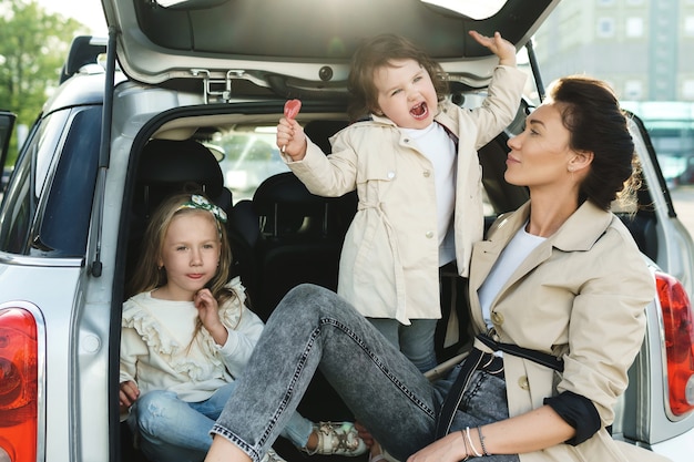 車のトランクに座っている若い母親と彼女の愛らしいdauthers。