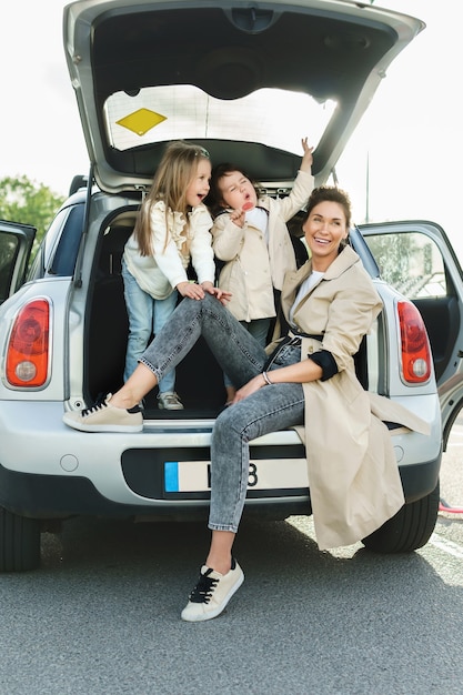 Young mother and her adorable dauthers sitting in a car trunk.