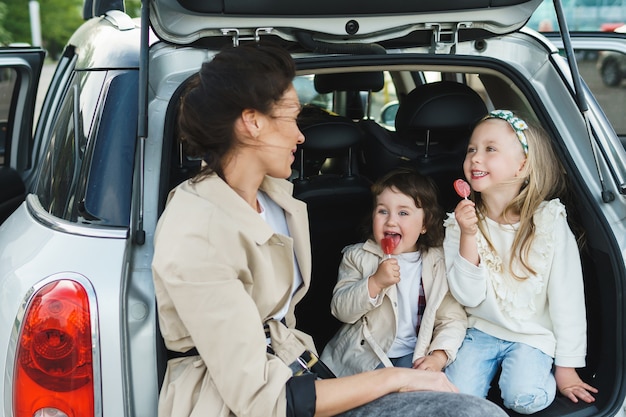 Young mother and her adorable dauthers sitting in a car trunk.