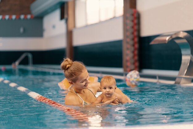 Young mother and her baby enjoying a baby swimming lesson in the pool. Child having fun in water with mom