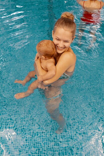 Young mother and her baby enjoying a baby swimming lesson in the pool. Child having fun in water with mom