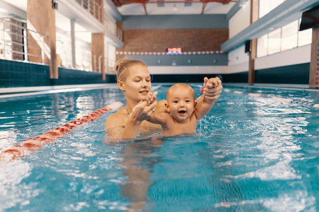 Young mother and her baby enjoying a baby swimming lesson in the pool. Child having fun in water with mom