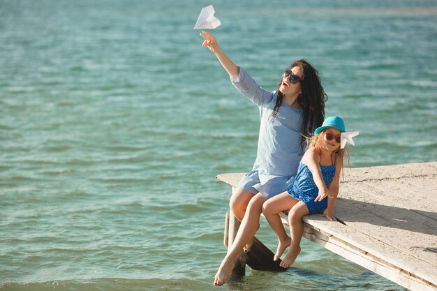 Young mother and her cute daughter at the sea side launching paper airplanes in the air and laughing