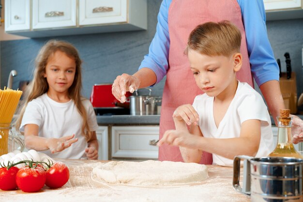 Foto giovane madre e i suoi bambini carini che cucinano pizza insieme