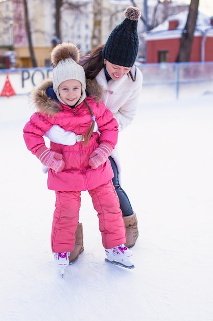 Young mother and her cute little daughter on a skating rink