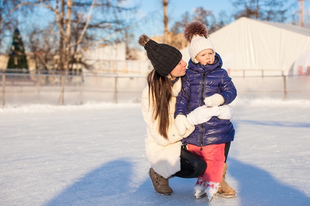 Young mother and her cute little daughter on a skating rink