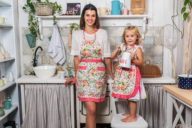 Молодая мать и ее дочь готовят на кухне в красивых фартуках