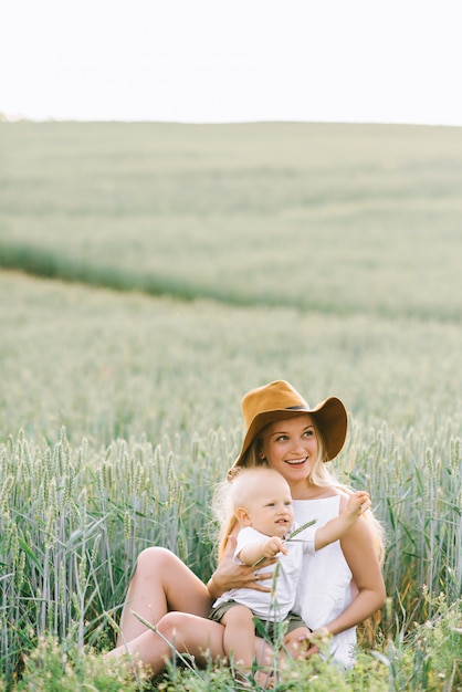 Una giovane madre e il suo piccolo bambino seduto vicino al grano su uno sfondo verde