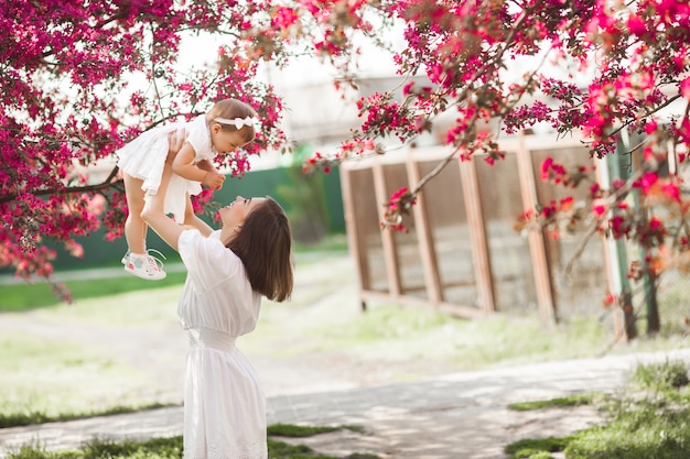 Young mother and her little daughter walking in the park together in the spring time. happy family outdoors. loving  with adorable baby girl.