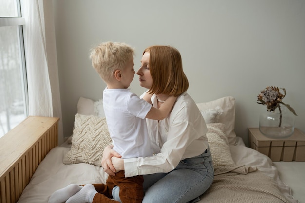 Young mother and her son spending time together at home sitting on bed